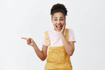 gosh-what-great-news-portrait-of-surprised-good-looking-amazed-female-in-yellow-stylish-dungarees-holding-palm-on-cheek-being-charmed-and-impressed-pointing-left-and-asking-question